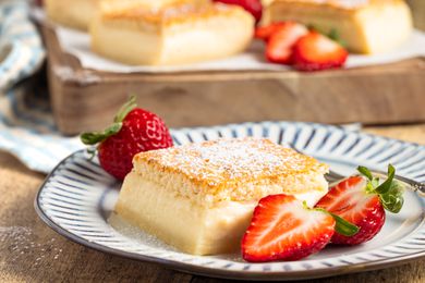 A serving of the magic cake recipe on a plate, with fresh strawberries around it for garnish