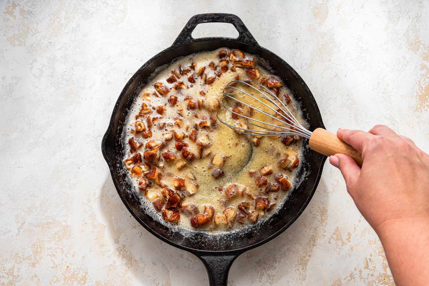 hand with whisk stirring buttery sauce and chopped mushrooms in a cast iron skillet