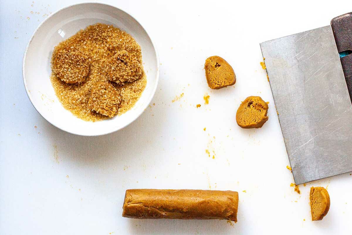 A log of Make Ahead SLice and Bake Ginger Cookies are being cut and rolled in raw sugar.