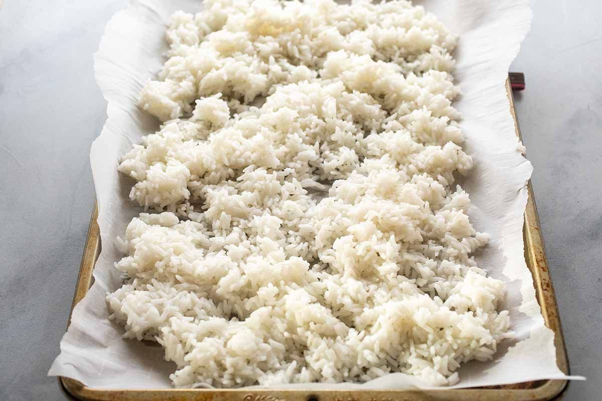 Cooked white rice spread on a baking sheet covered in parchment paper for Pork Fried Rice recipe.