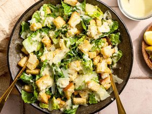 Caesar salad with croutons and Parmesan in a bowl with dressing and lemon on the side