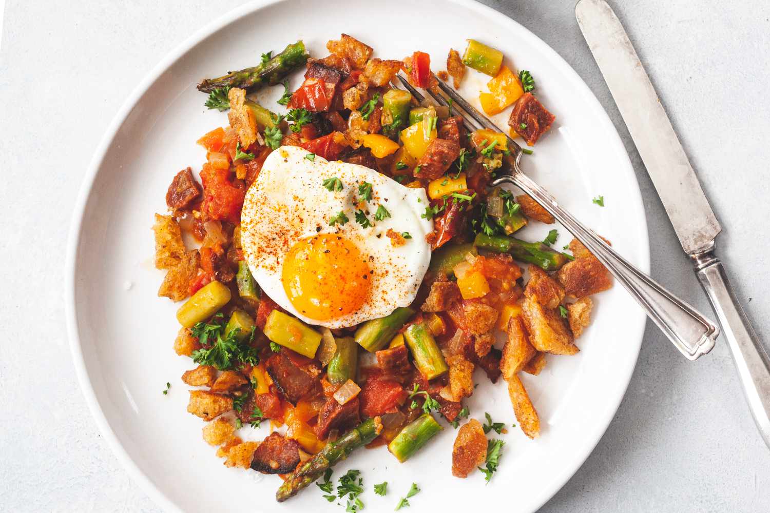 Overhead view of a white plate with Spanish Style Migas with Asparagus, Chorizo, Bacon, and Eggs.