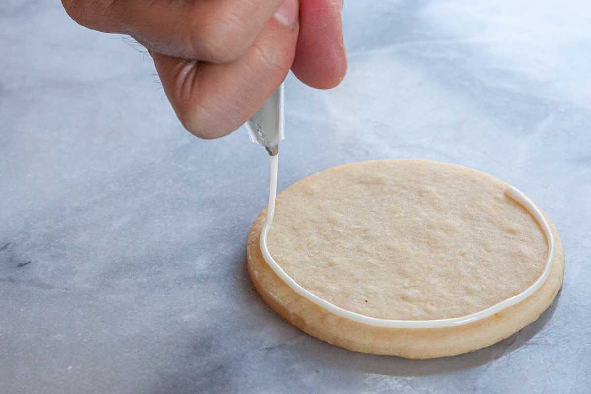 A circle sugar cookie is outlined with white royal icing.