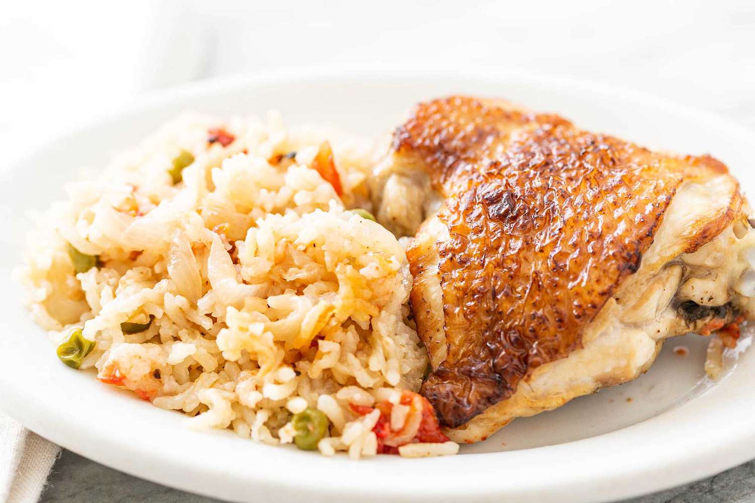 A golden brown chicken thigh and rice sit atop a white plate.