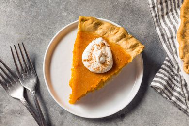 Overhead view of a white plate of homemade sweet potato thanksgiving pie next to two forks and a striped napkin and edge of a full pie