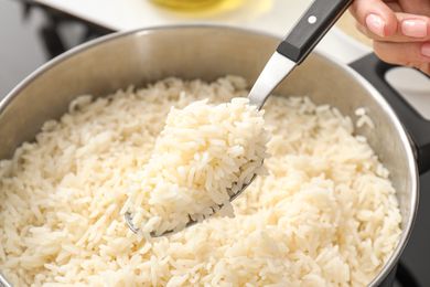 Closeup of a spoon with cooked rice above a pot with cooked rice