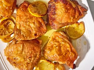 Overhead closeup view of a white serving platter of lemon chicken thighs and lemon slices