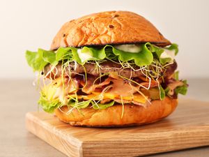 A gourmet burger with lettuce, sprouts, cheese, and mayo on a wooden surface