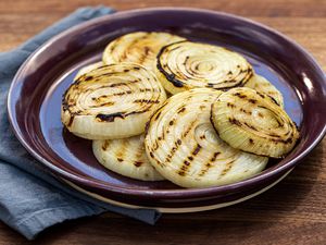 The best ever grilled onions piled on a purple rimmed platter.