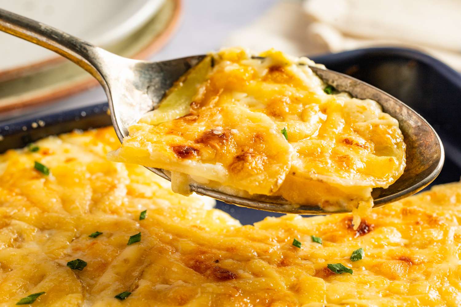 Closeup view of a spoon with a serving of Sheet Pan Au Gratin Potatoes recipe