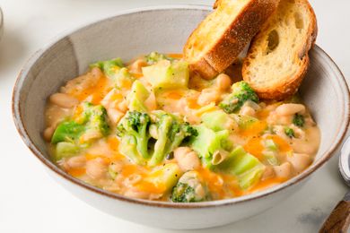 Angled view of a stoneware bowl of Broccoli Cheddar Creamy Beans next to a spoon and all on a white background