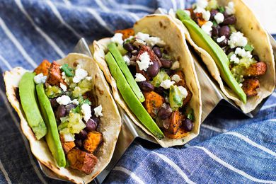 a row of Sweet Potato Black Bean Tacos topped with avocado, cotija cheese, and salsa verde
