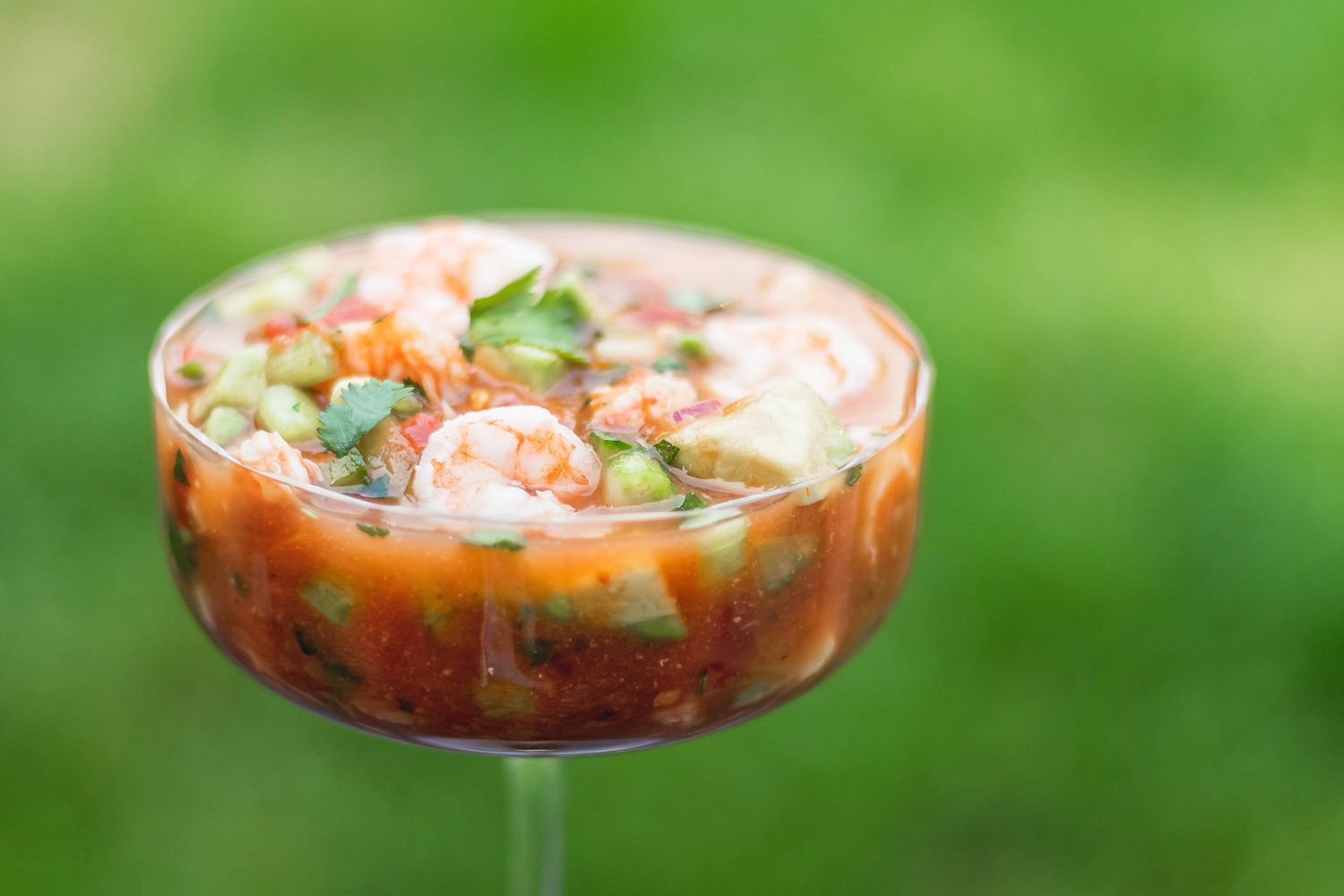 A wine glass with mexican shrimp cocktail set on a table outside.