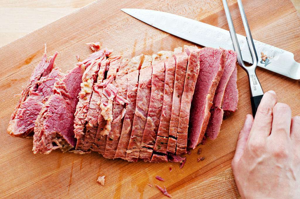 Sliced corned beef on cutting board with a meat fork and knife