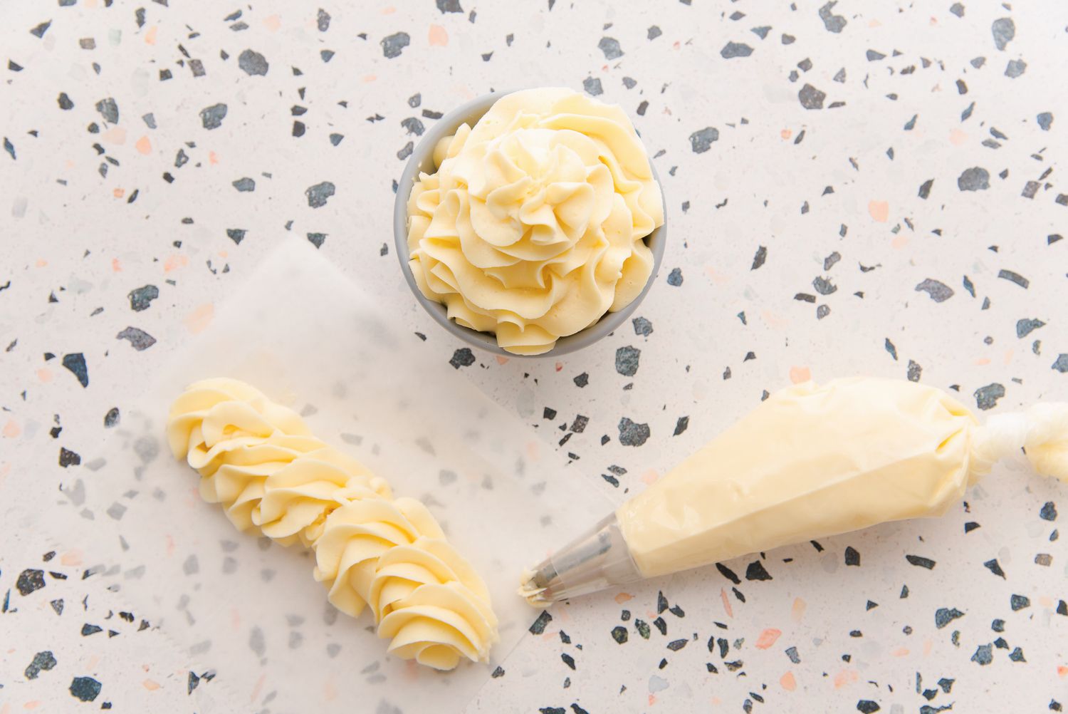 German buttercream piped on parchment paper, in a piping bag, and piped into a bowl.