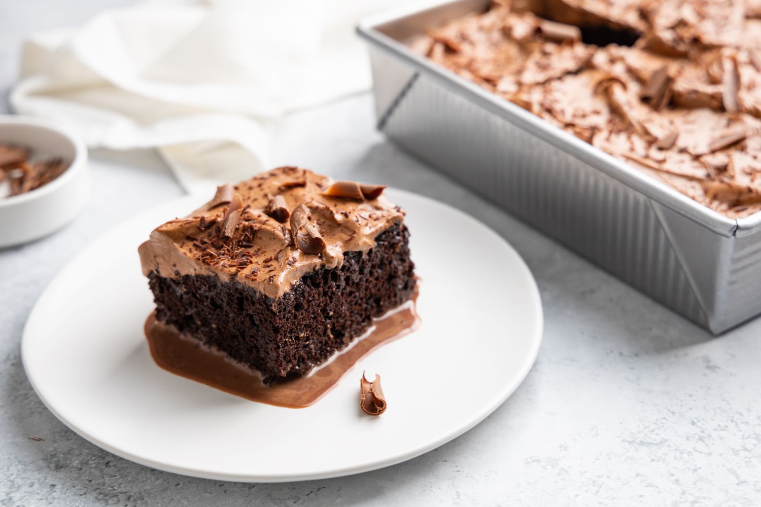 Slice of Chocolate Tres Leches Cake on a Small Plate with More in the Cake Pan Next to It