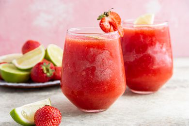 Frozen Strawberry Daiquiri in Stemless Wine Glasses Next to a Sliced Limes and Strawberries