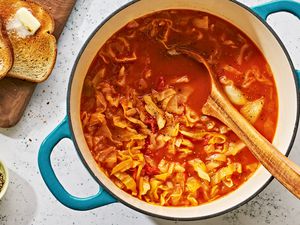 A pot of cabbage soup with wooden a spoon in it and toast on the side