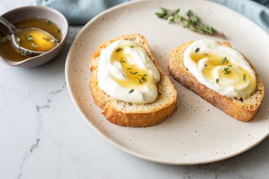 Two Pieces of Whipped Ricotta Toast Topped with Lemon-Thyme Honey Next to a Bowl of More Honey