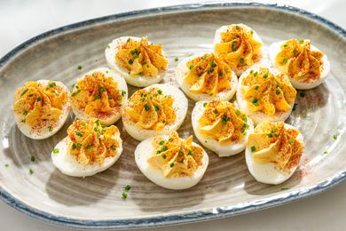 A ceramic serving plate with deviled eggs, garnished with chopped chives and paprika