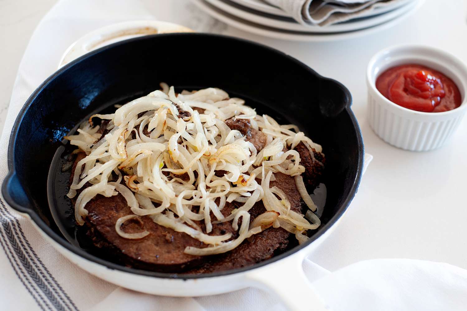 A skillet with liver and onions recipe and ketchup.