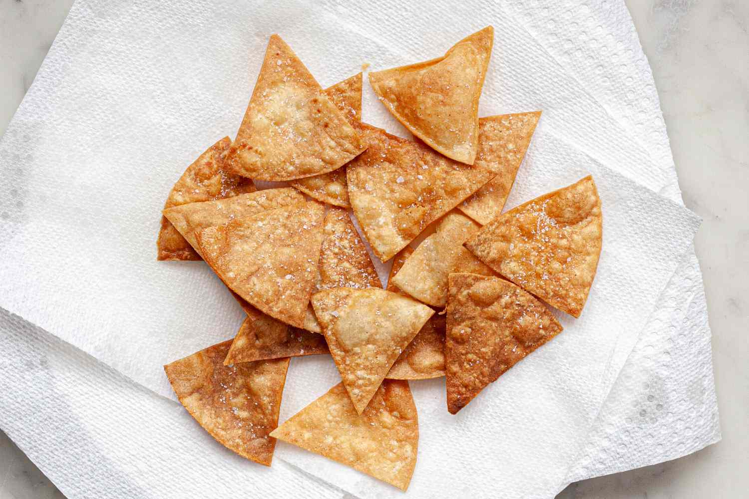 Crispy homemade tortilla chips draining on paper towels.