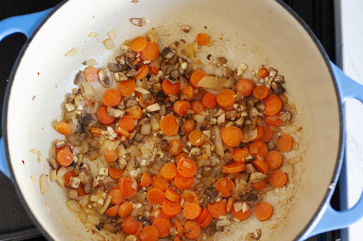 Dutch oven with sliced carrots and onions cooking in a dutch oven on the stove.