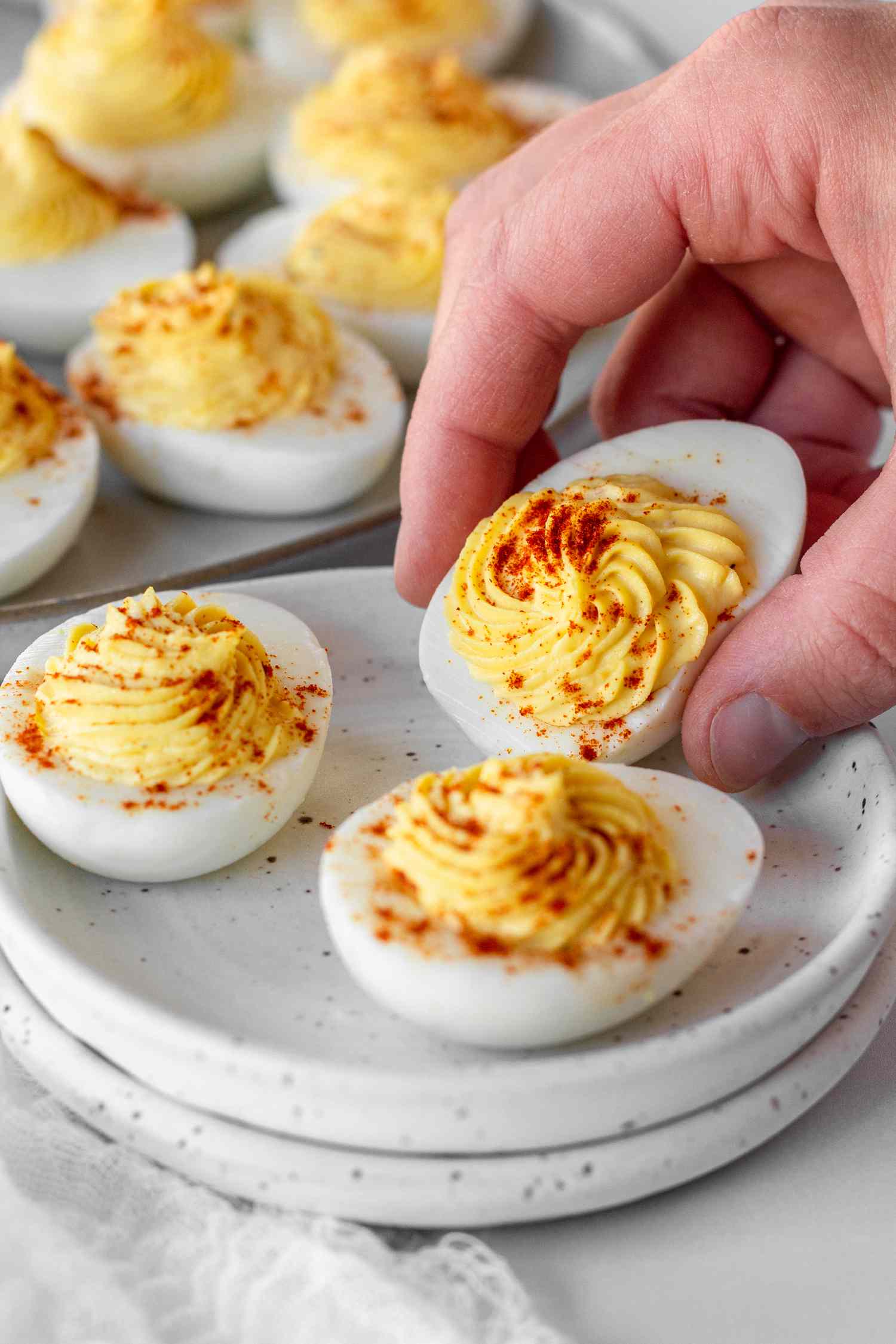 A hand picking up a Classic Deviled Egg off a small plate.