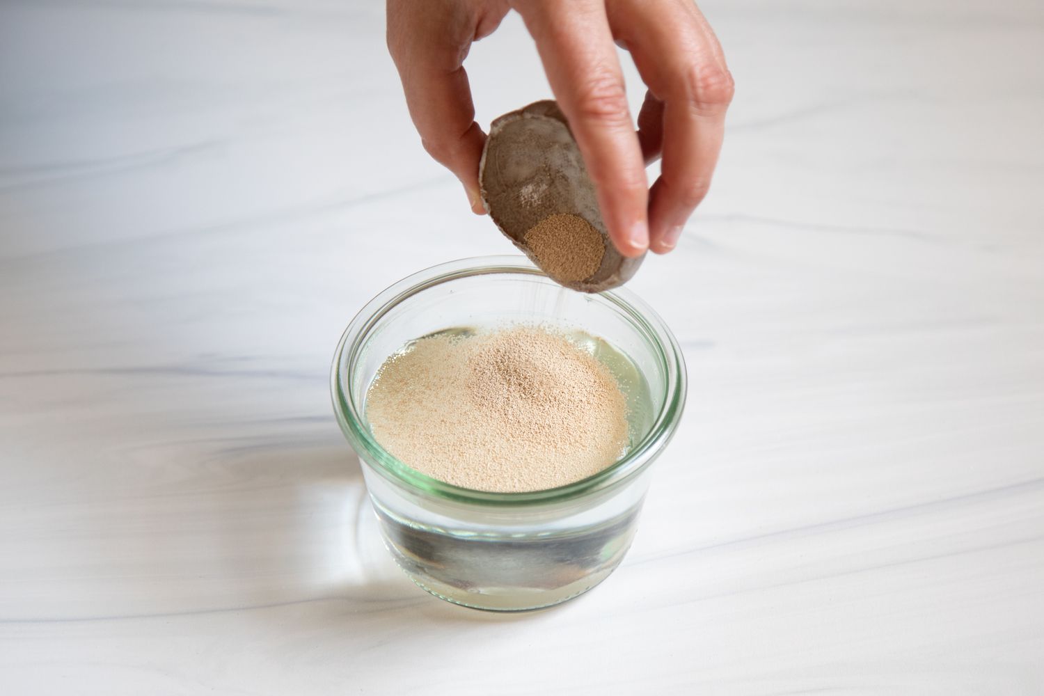 Pouring dry yeast into a cup of water.