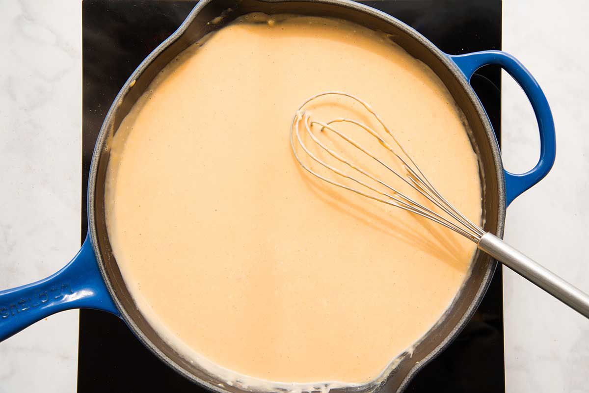 A black cast iron skillet will spices, milk and cheese being whisked together with a wooden spoon for easy homemade queso