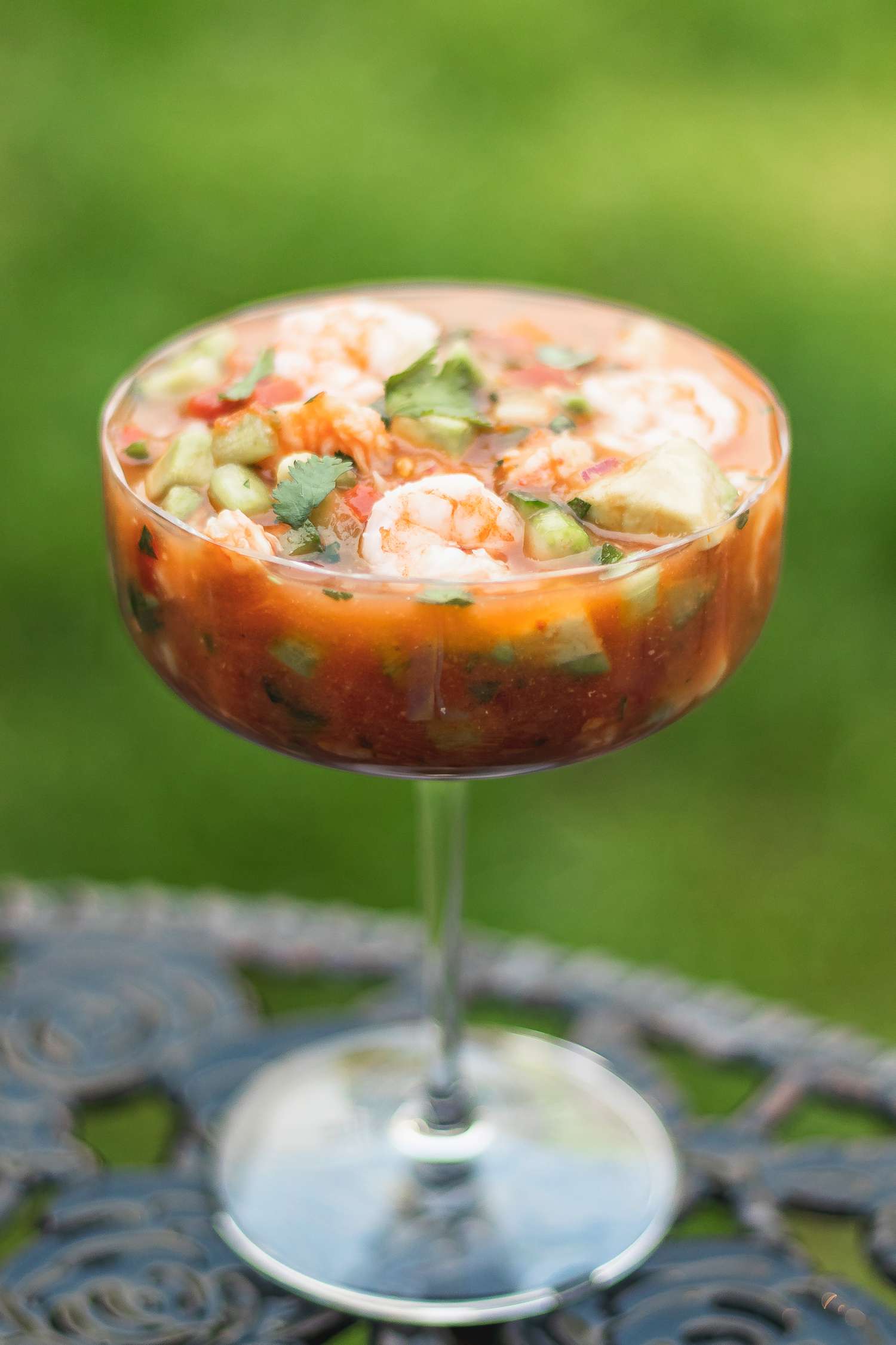A parfait glass with mexican shrimp cocktail set on a table outside.