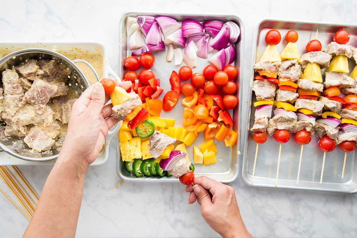 Garlic and citrus grilled pork kebabs being assembled and the finished kebabs are put on a sheet pan.