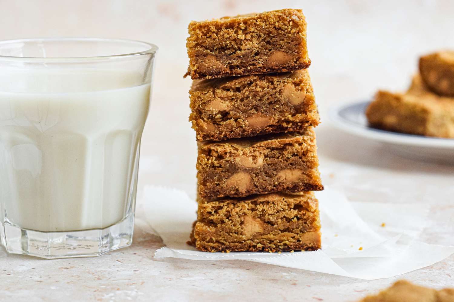 Side view of blonde brownies in a stack with a glass of milk