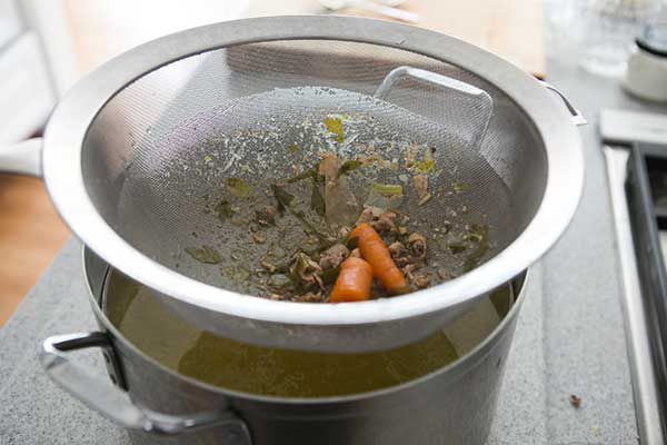 Straining solid pieces out of cooked chicken broth