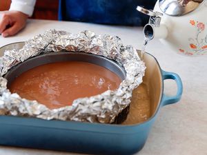 Chocolate cheesecake in waterbath. Person holding tea kettle with water to illustrate how to save a cheesecake if it gets wet.