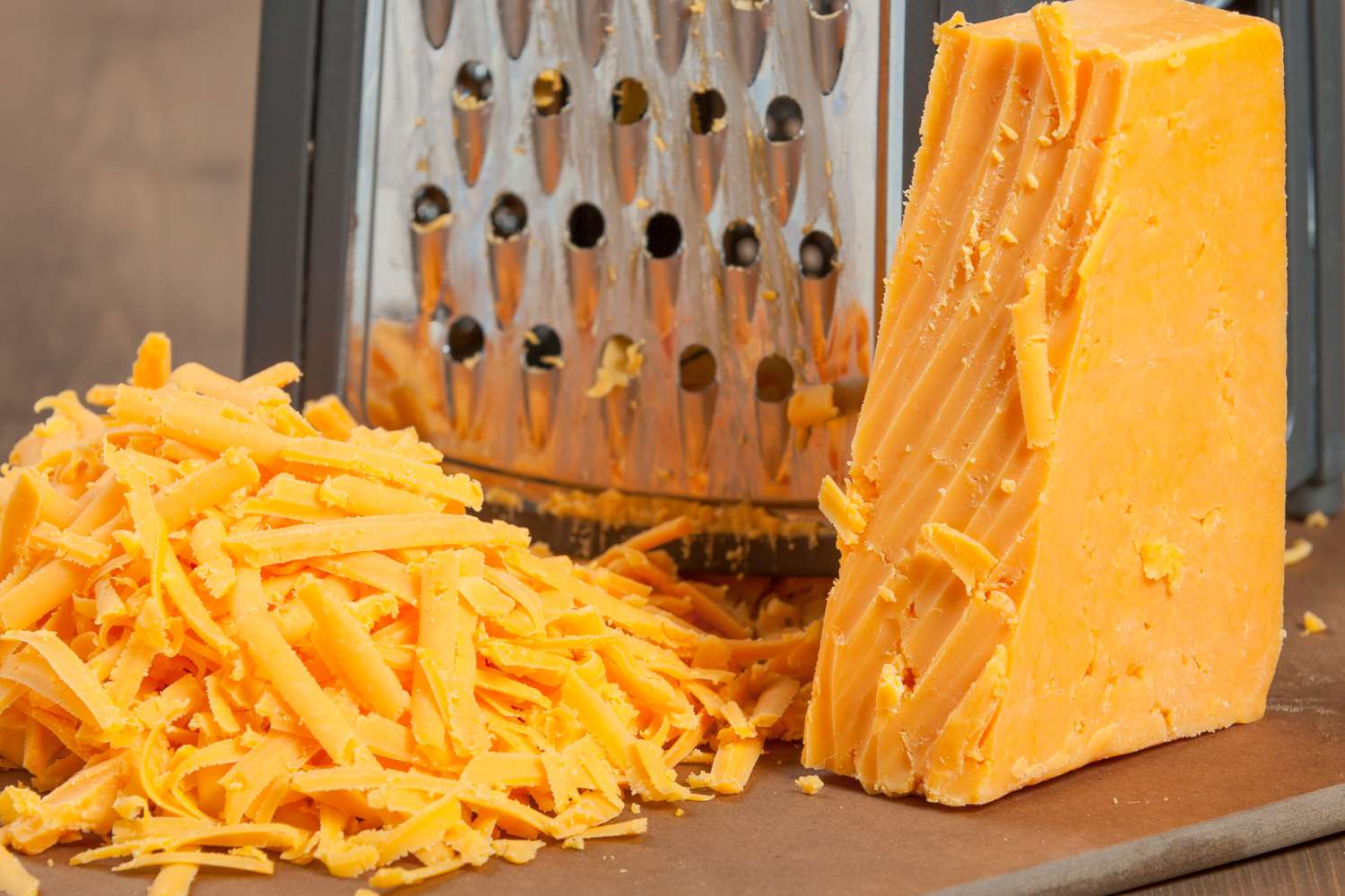 Close up of a partially shredded block of orange cheddar with a cheese grater in the background