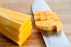 A knife cutting butternut squash being into cubes