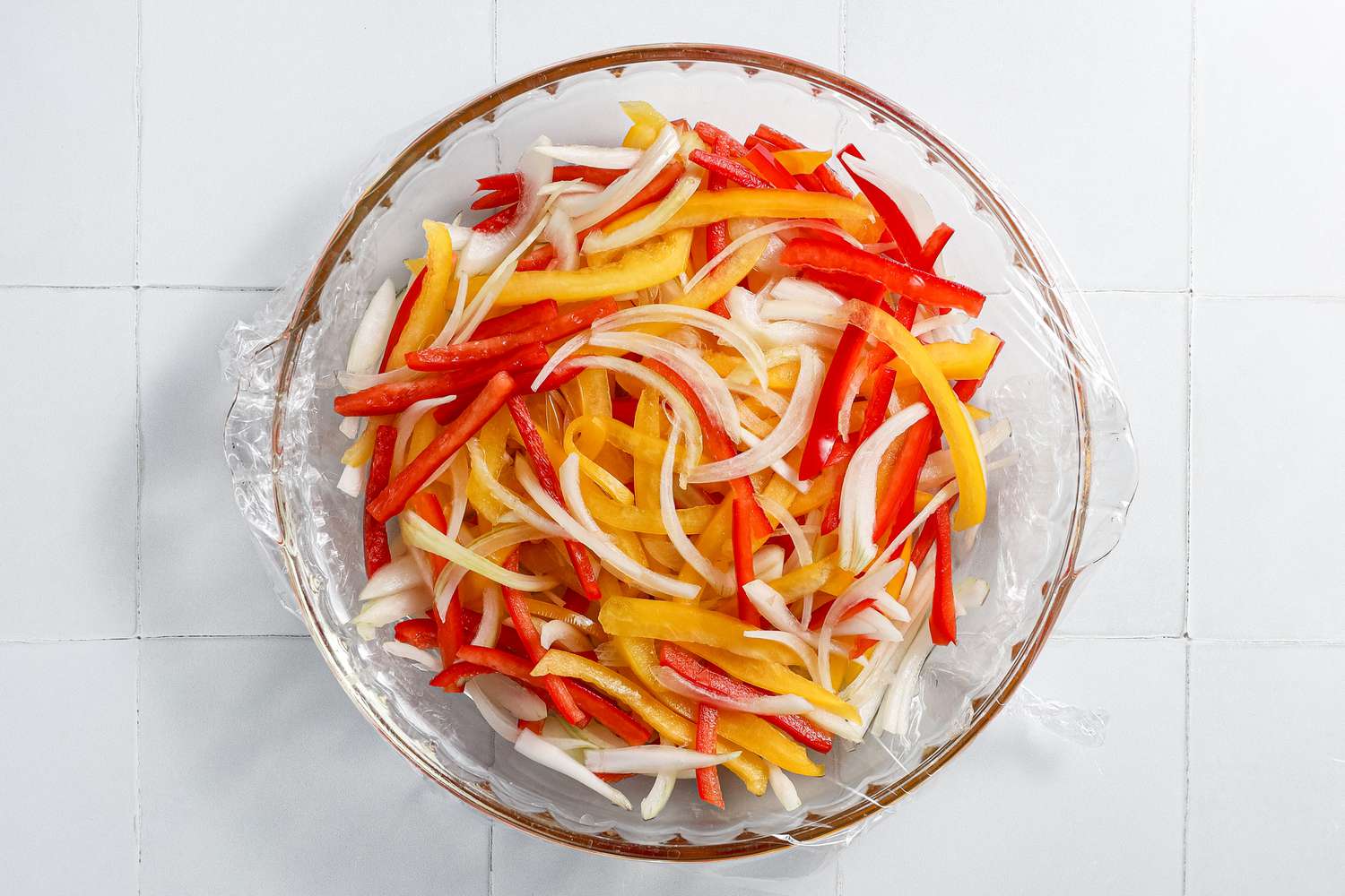 Sliced Onions and Bell Peppers in a Glass Pyrex Dish Covered in Plastic Wrap for Microwave Shakshuka Recipe 