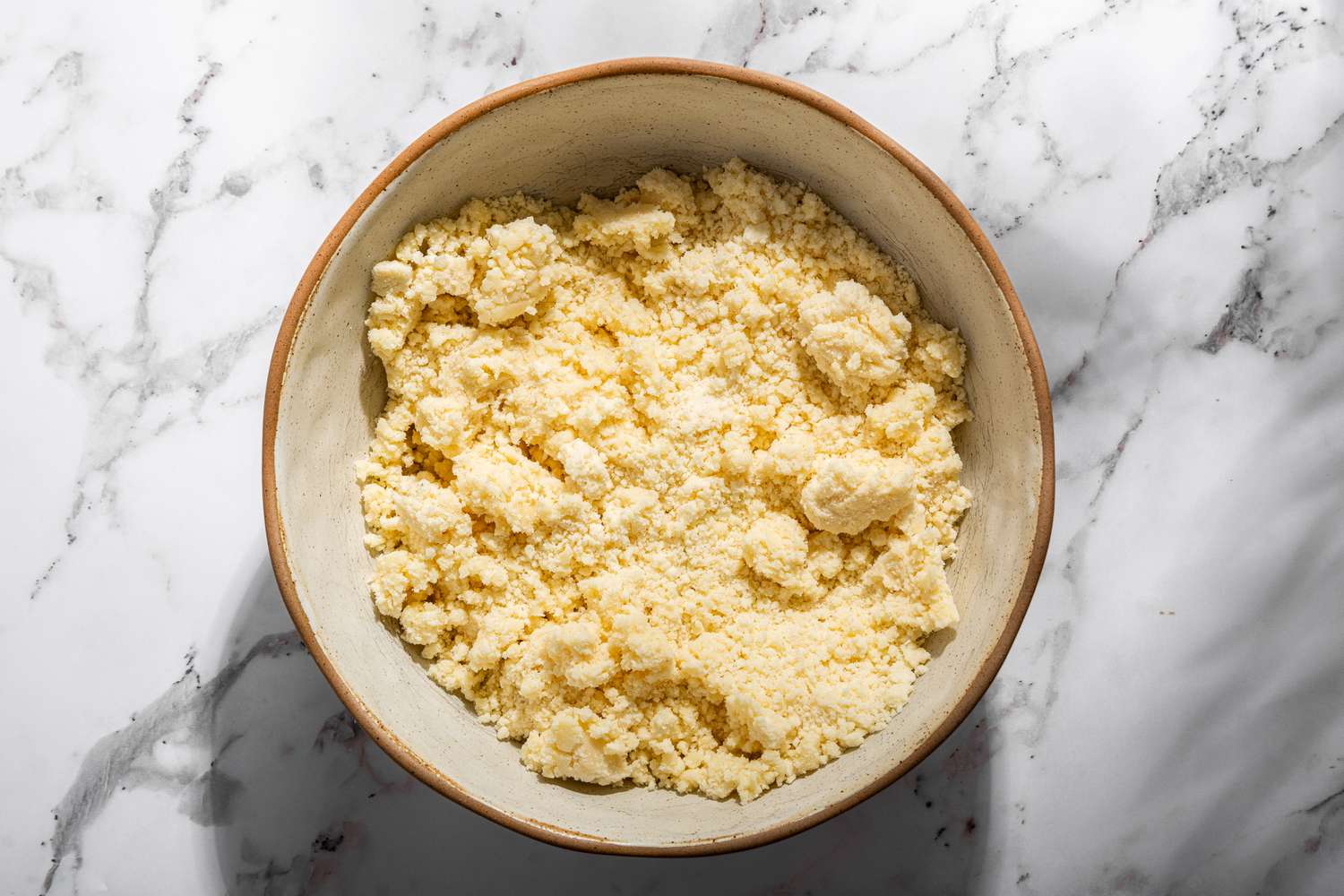 Overhead view of a bowl of flour, butter, and powdered sugar after pulsing together in a food processor for Millionaire Shortbread recipe 
