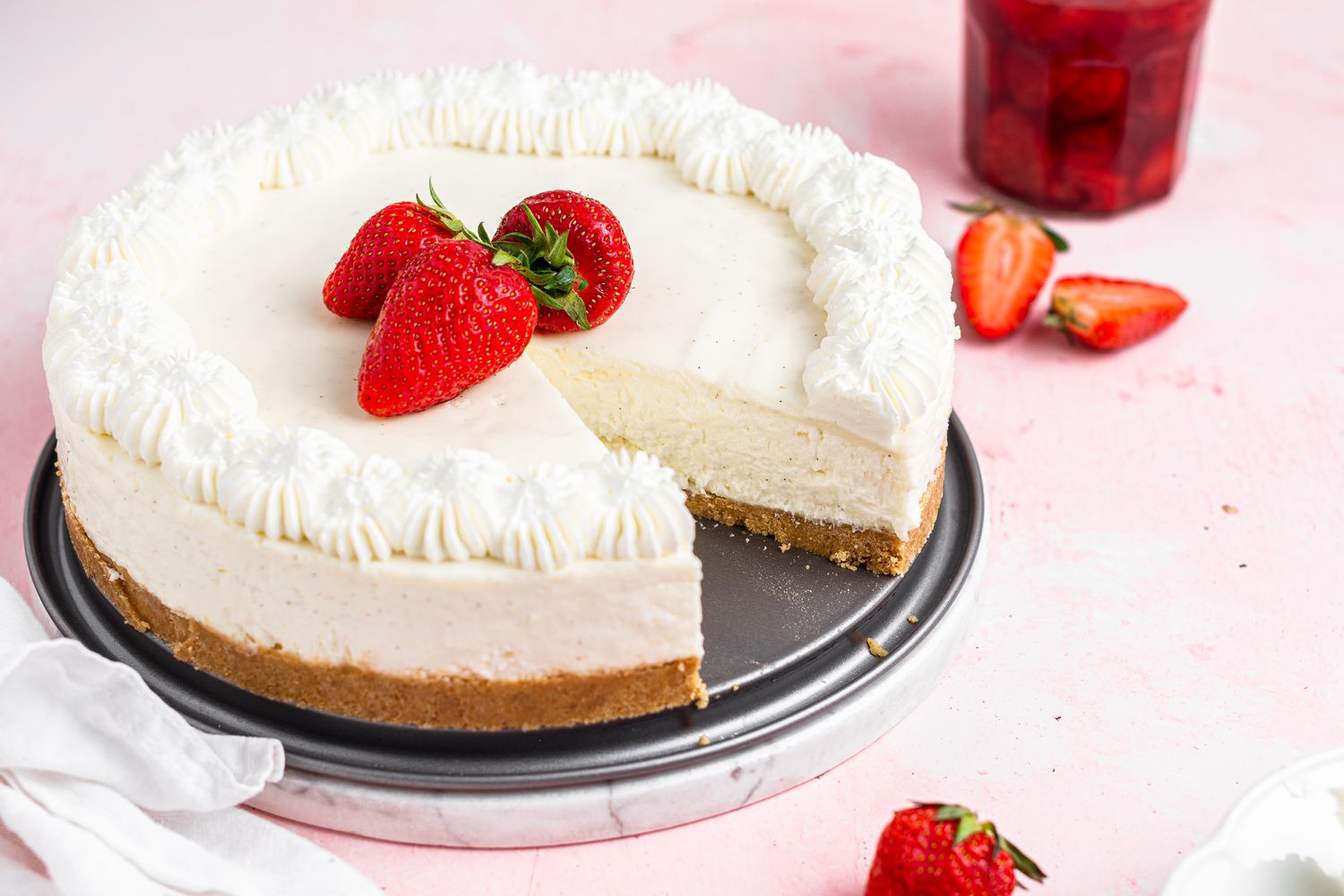 An easy no bake cheesecake with a slice removed and set on a pink background.
