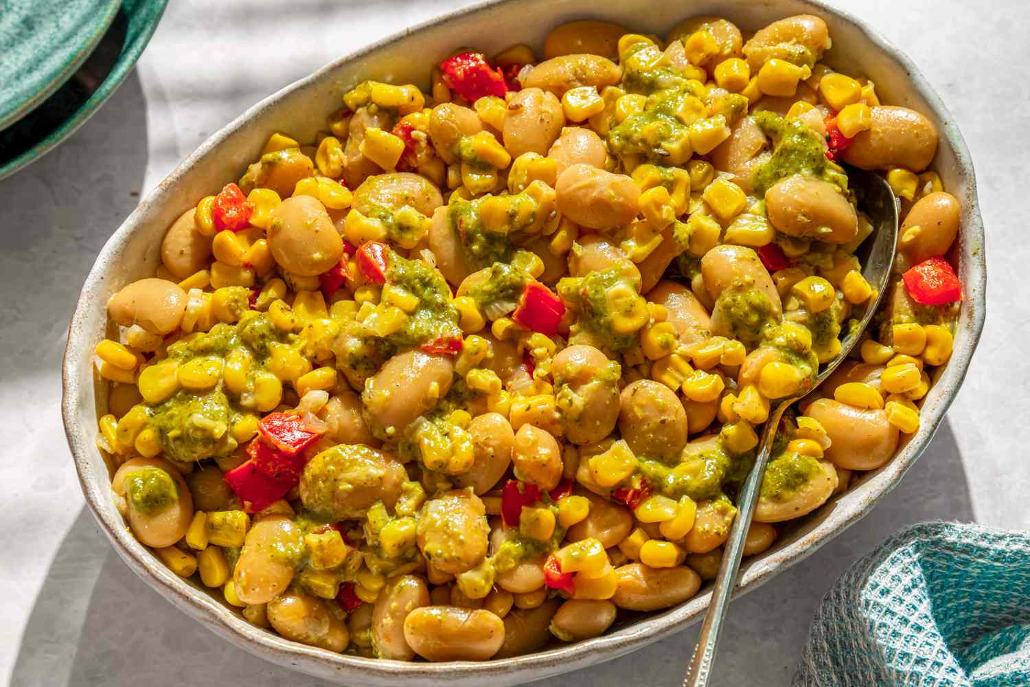 A serving of succotash with beans, corn, and diced vegetables, garnished with a green-colored sauce, in a white dish