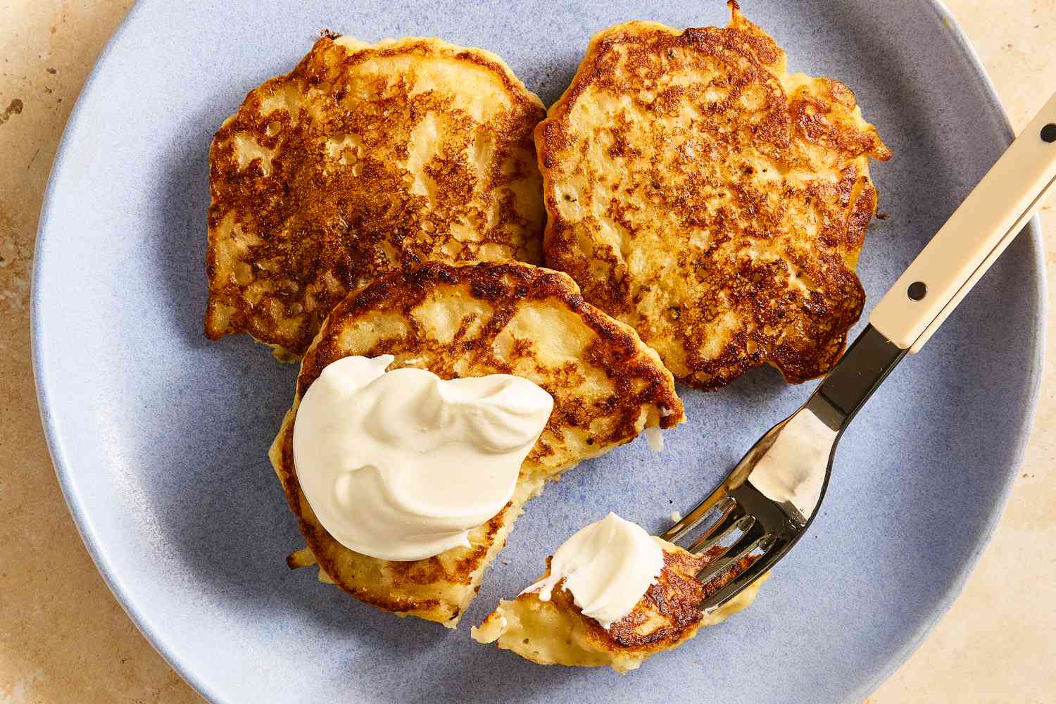 Overhead view of a plate of three potato pancakes with one topped with butter next to a fork holding a bite all on a stone countertop