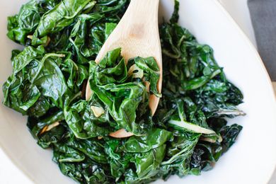 Wooden spoon scooping up cooked spinach recipe.