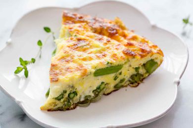 A slice of asparagus Frittata on a white scalloped plate