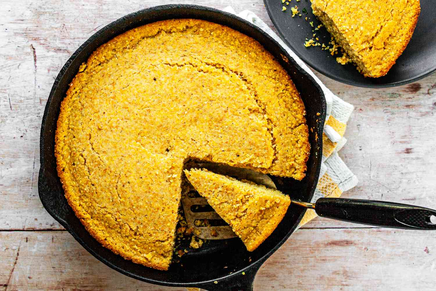 Southern Cornbread in a Skillet with a Piece Cut Out and Another Piece on a Plate