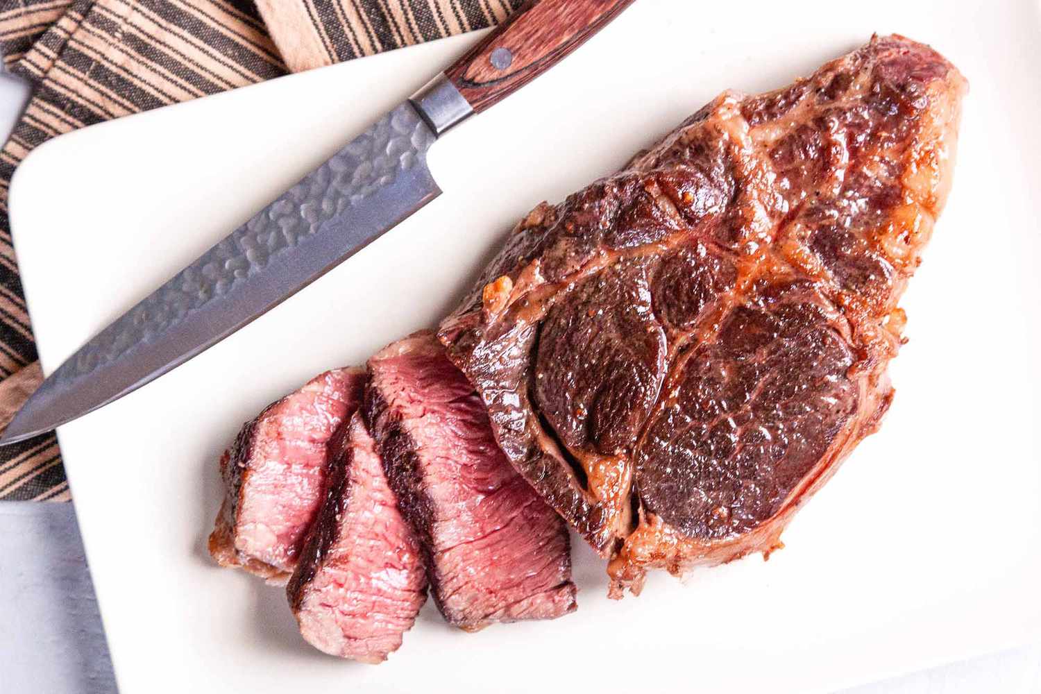 steak with a knife on a white cutting board