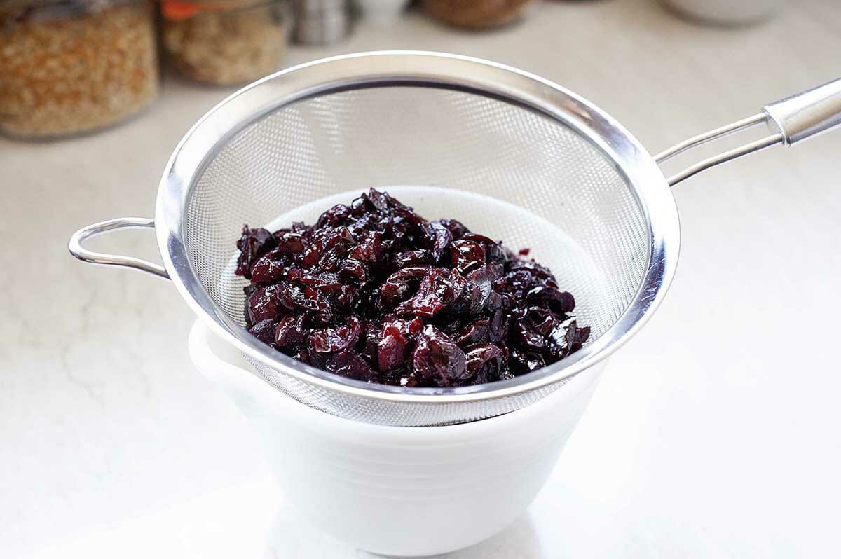 Stewed cherries strained and the liquid reserved in a white bowl.