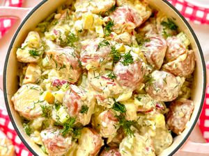 A prepared potato salad served in a pot, garnished with herbs and diced vegetables