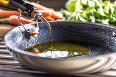 Sideview of oil getting poured into a nonstick pan