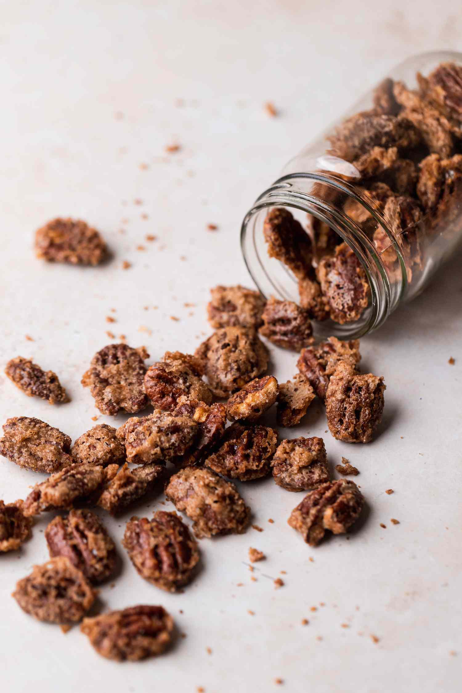 A glass jar tipped over with sugared pecans spilling out from it.